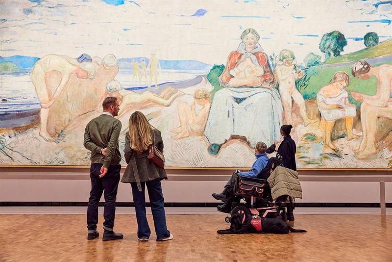 Fire personer, en i rullestol, og hund som ser på et stort veggmaleri