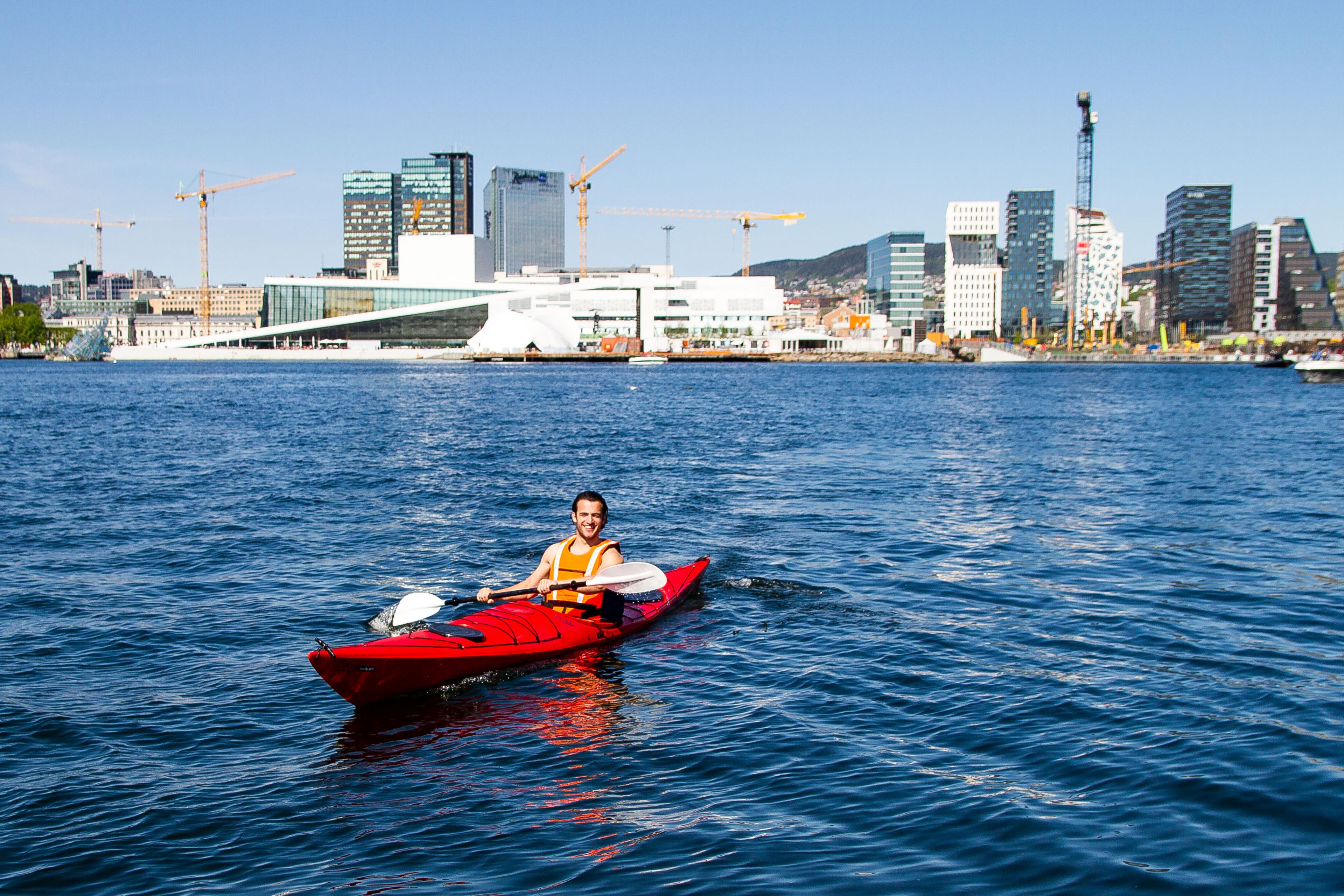 A man sitting in a red kayak in front of the Opera House and Barcode.