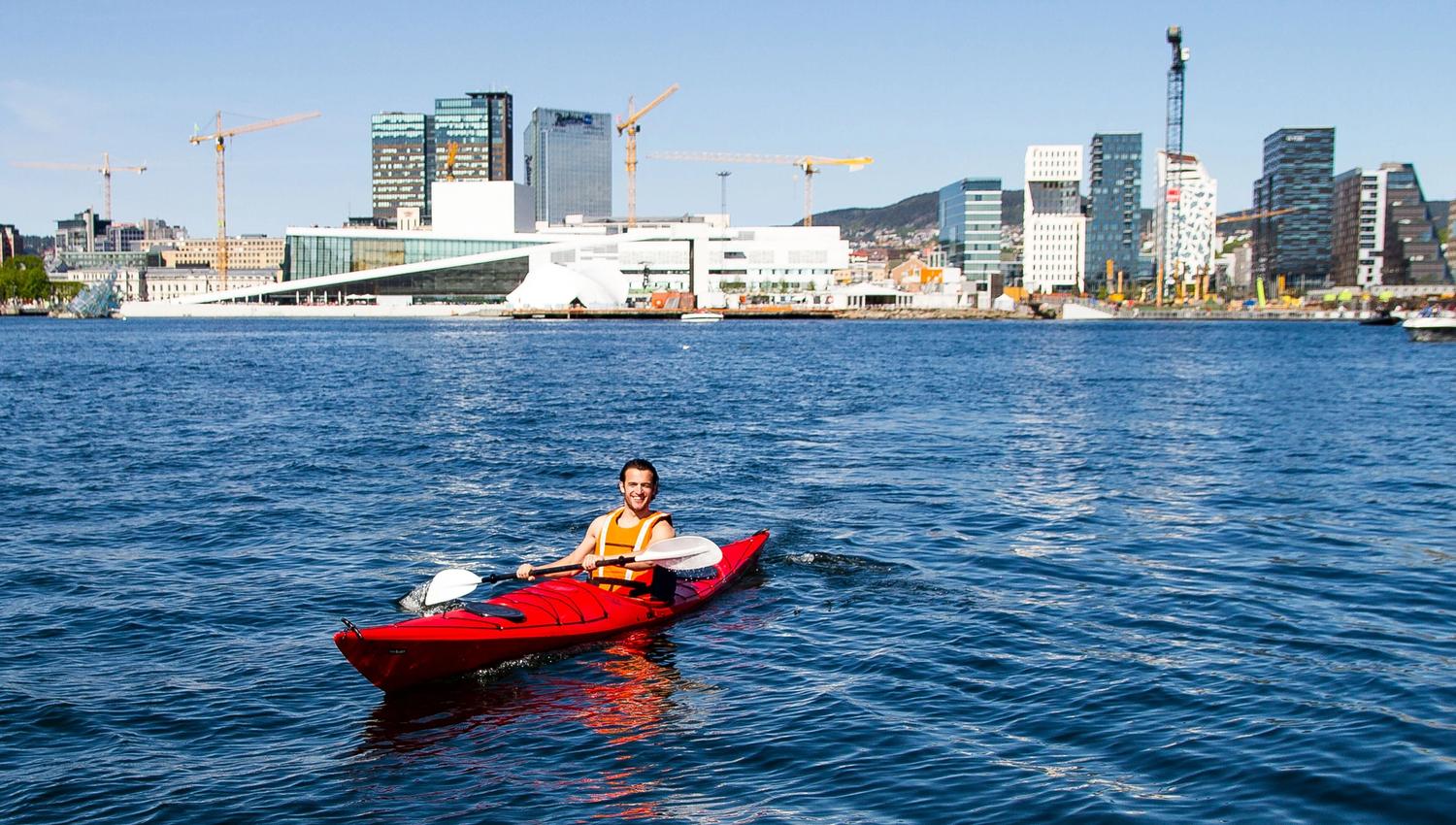 A man sitting in a red kayak in front of the Opera House and Barcode.