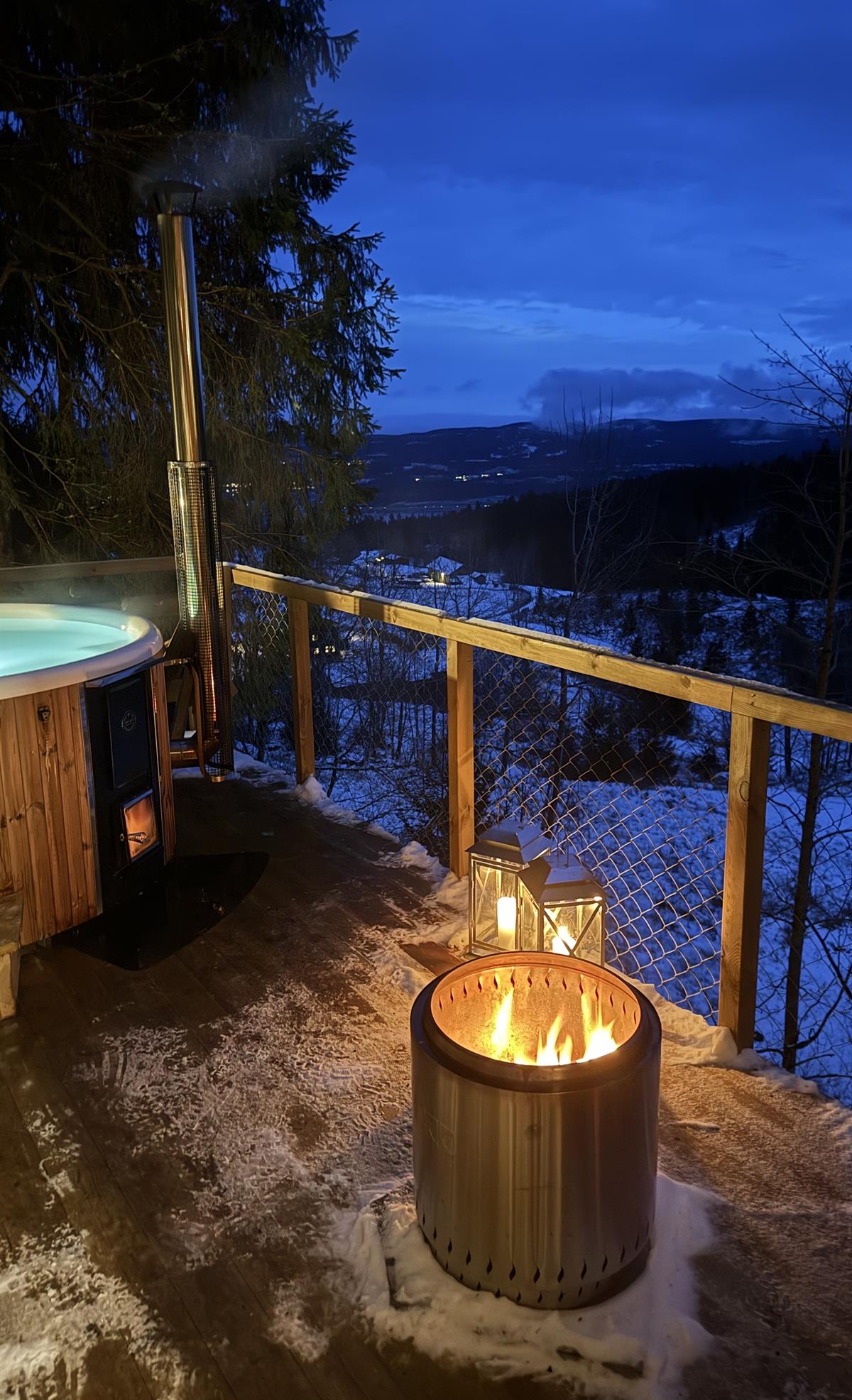 Outdoor area with a small wooden cabin and a fire pit, photographed at dusk with a view toward water and forest.