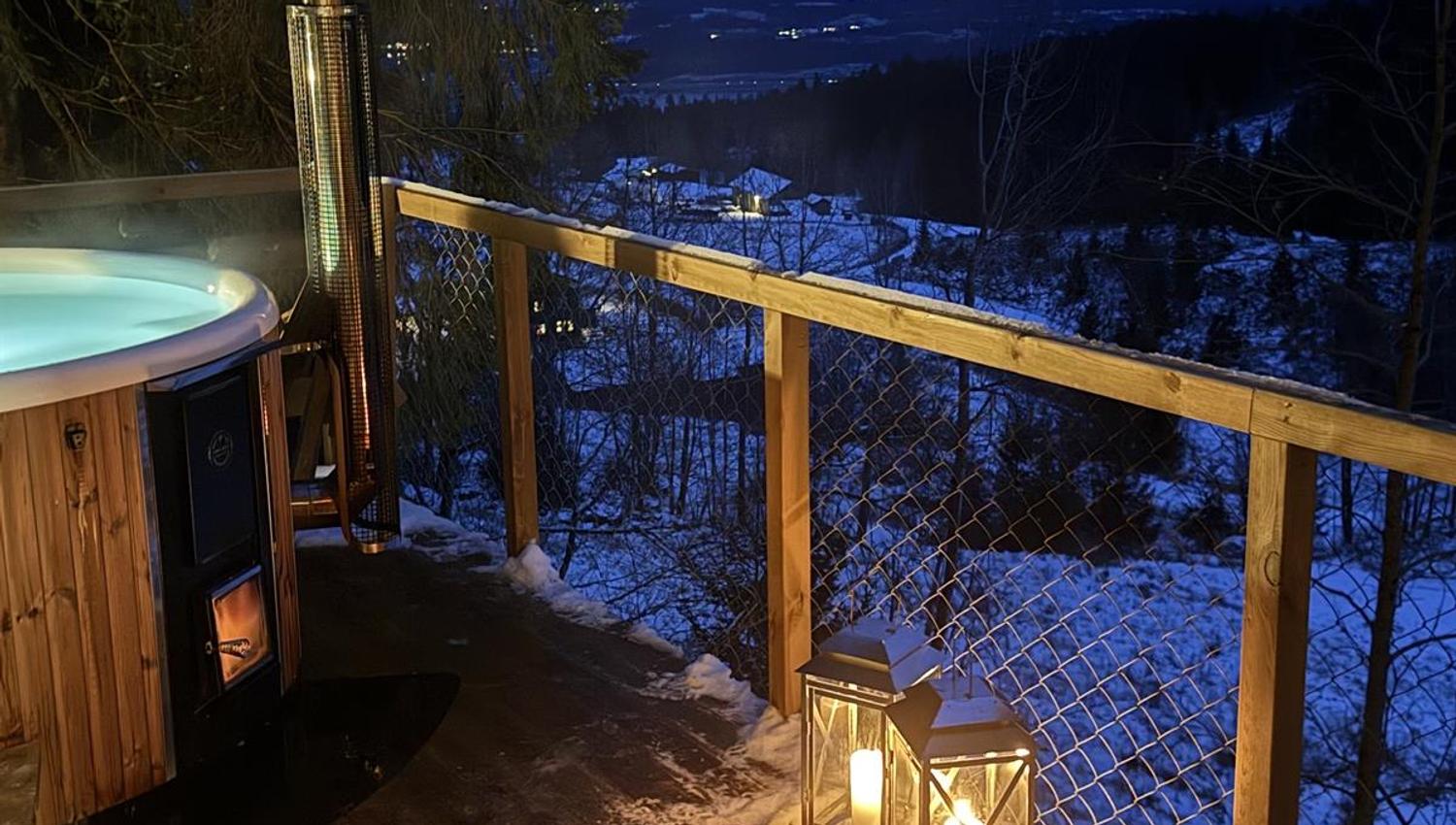 Outdoor area with a small wooden cabin and a fire pit, photographed at dusk with a view toward water and forest.
