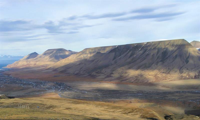 Grønt gress og en liten elv i en dal omringet av høye fjell i bakgrunnen