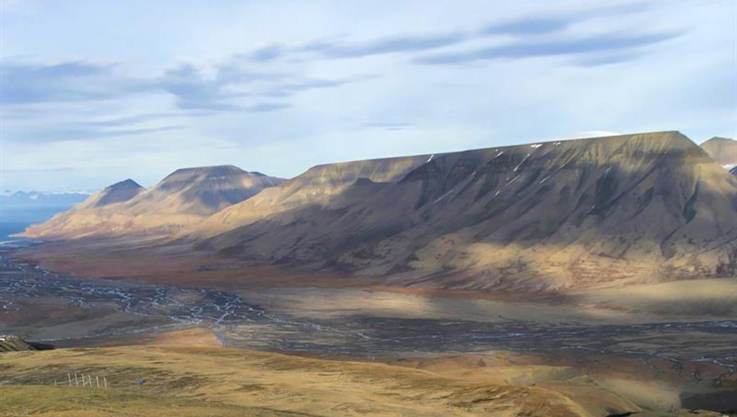 Grønt gress og en liten elv i en dal omringet av høye fjell i bakgrunnen