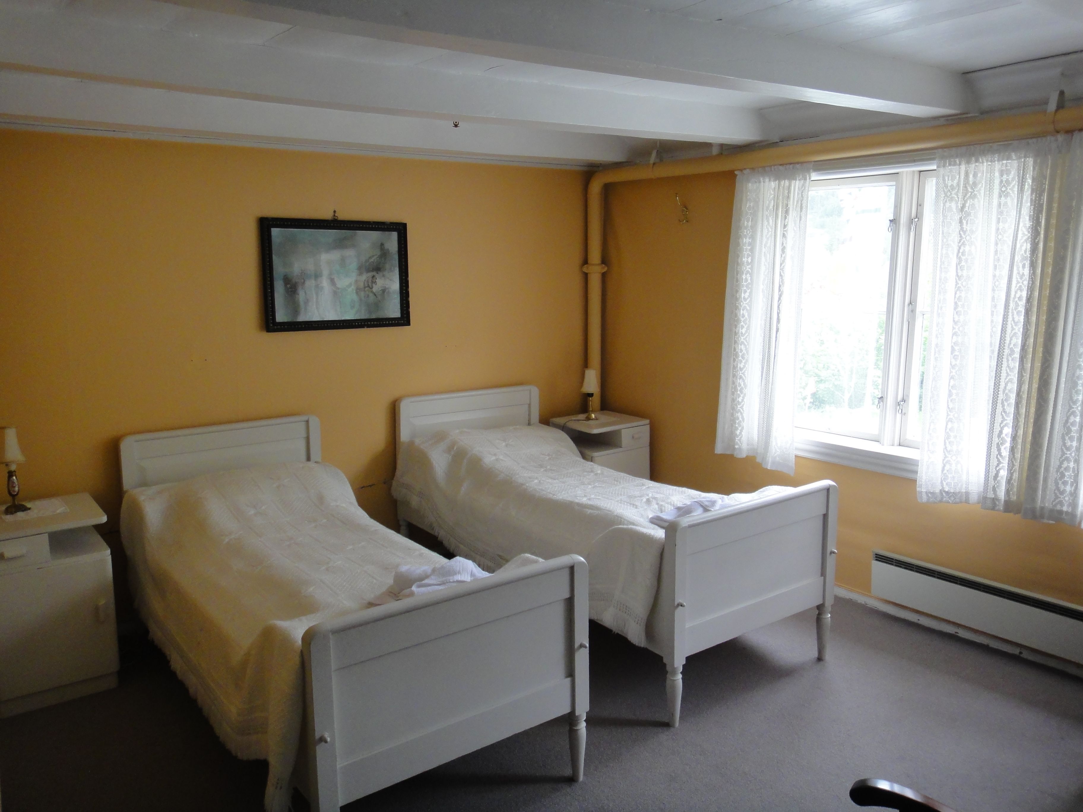 Tradisjonelt soverom med to kvite senger og store vindauge på Jaunsen Gjestgjevarstad i Hardanger.