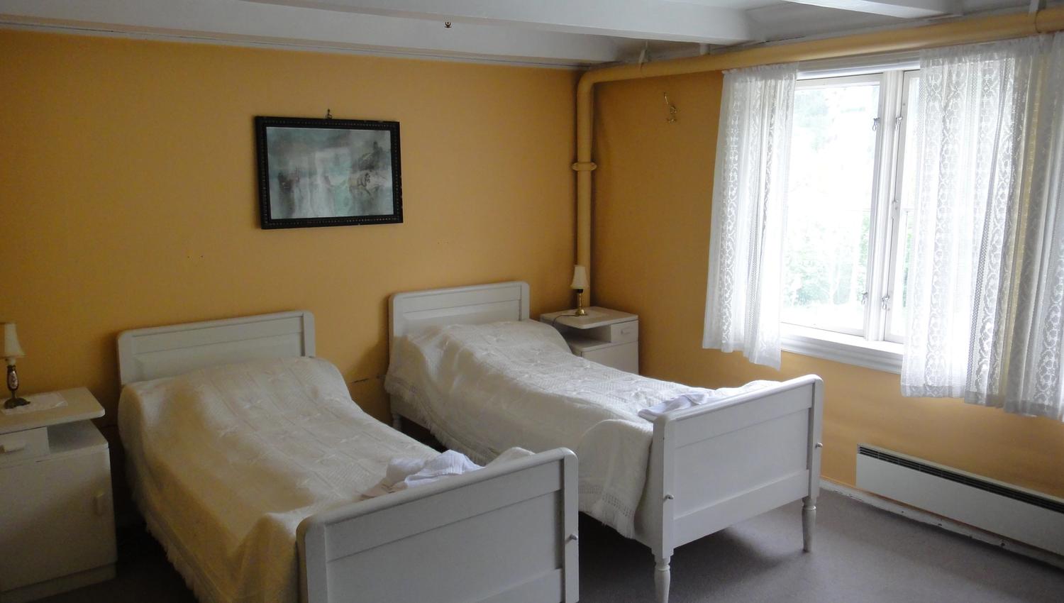 Traditional bedroom with two white beds and large windows at Jaunsen Guesthouse in Hardanger, Norway.