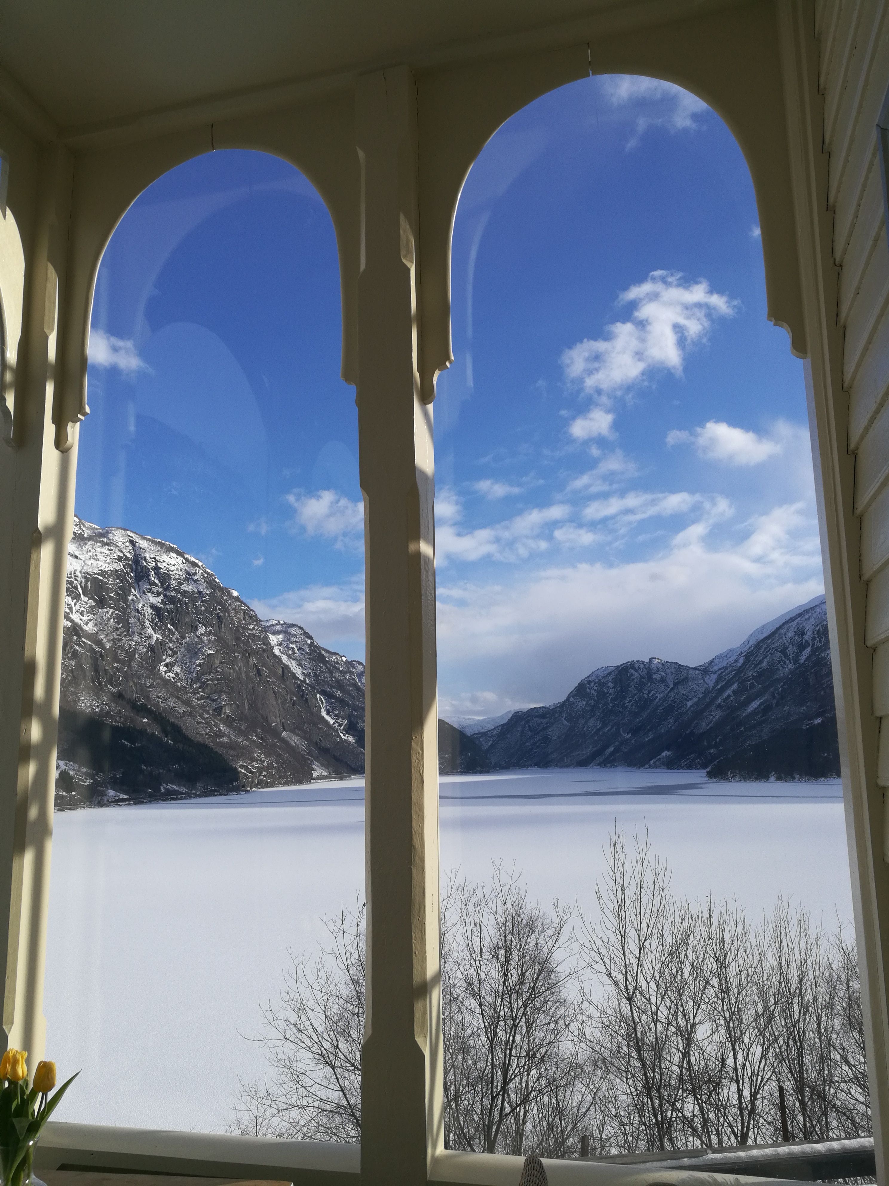 Fantastisk vinterutsikt frå verandaen på Vikinghaug Apartments, med snødekte fjell og ein stille fjord under blå himmel.