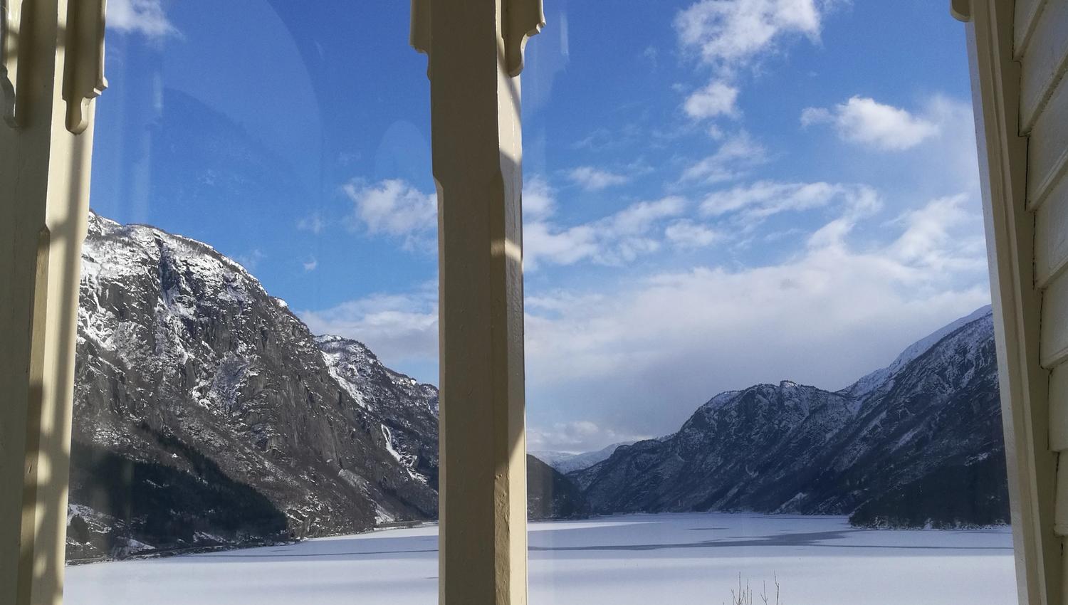 Fantastisk vinterutsikt frå verandaen på Vikinghaug Apartments, med snødekte fjell og ein stille fjord under blå himmel.