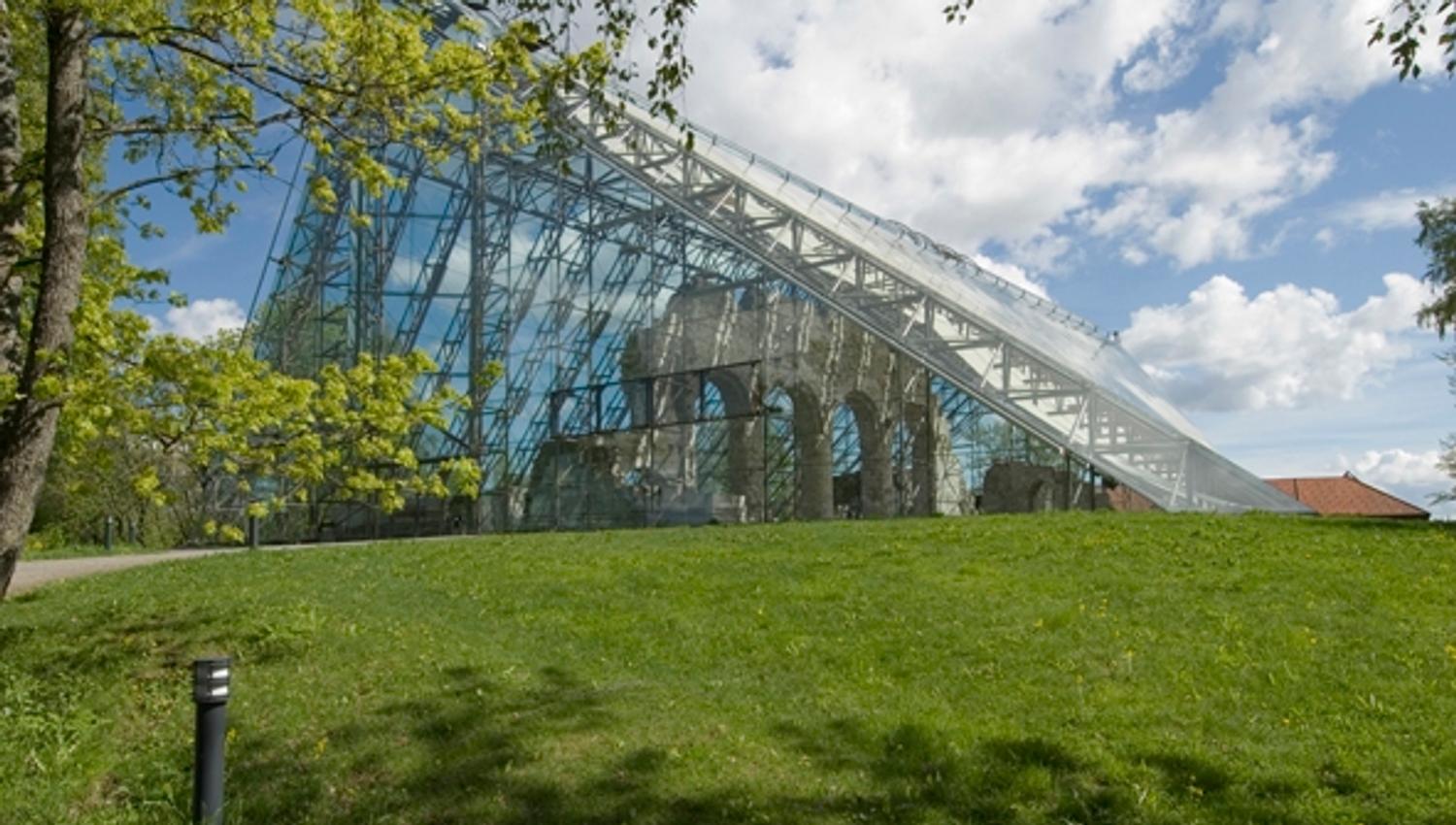 Hamardomen på Domkirkeodden
En stor bygning med glassfasade ligger bak en gressbakke under blå himmel og skyer.