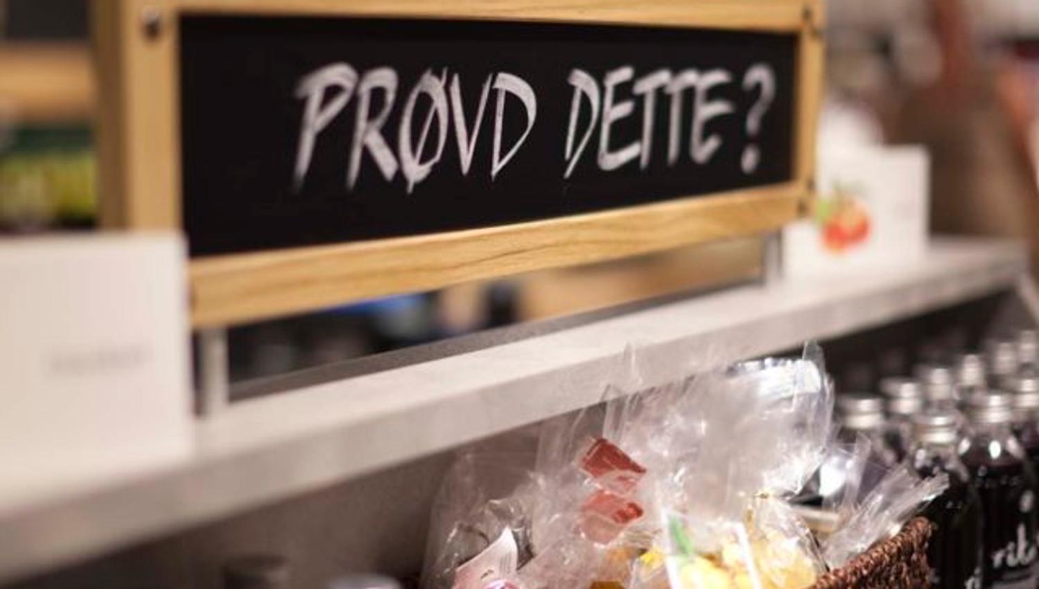 Et skilt med teksten «Prøvd dette?» står over en butikkhylle med flasker og poser med varer. Skiltet inviterer kunder til å teste eller kjøpe noe nytt.