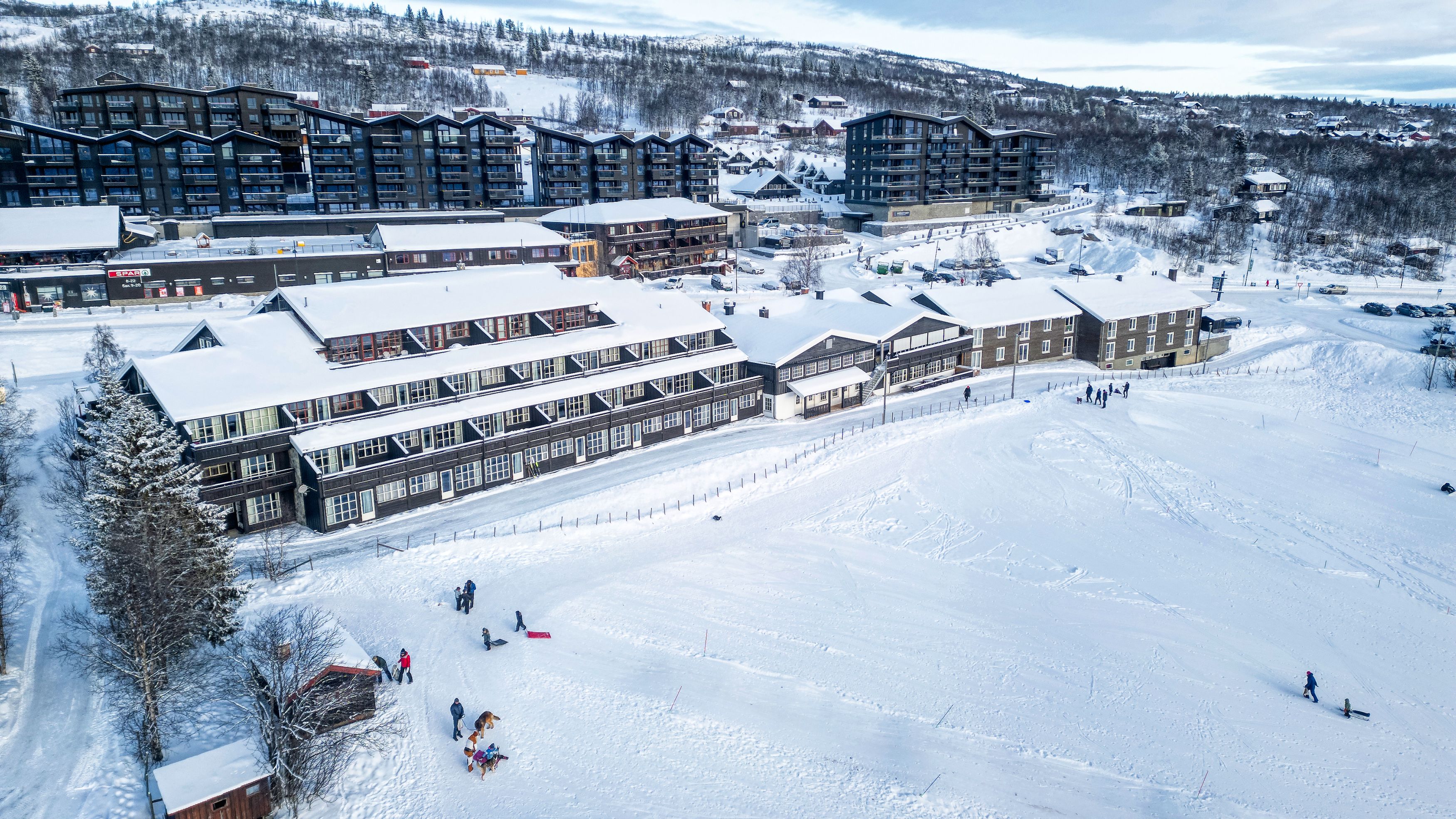 Dronebilde av Bergo Rom på vinteren. Man kan se barn som aker på jordet en fin vinterdag.