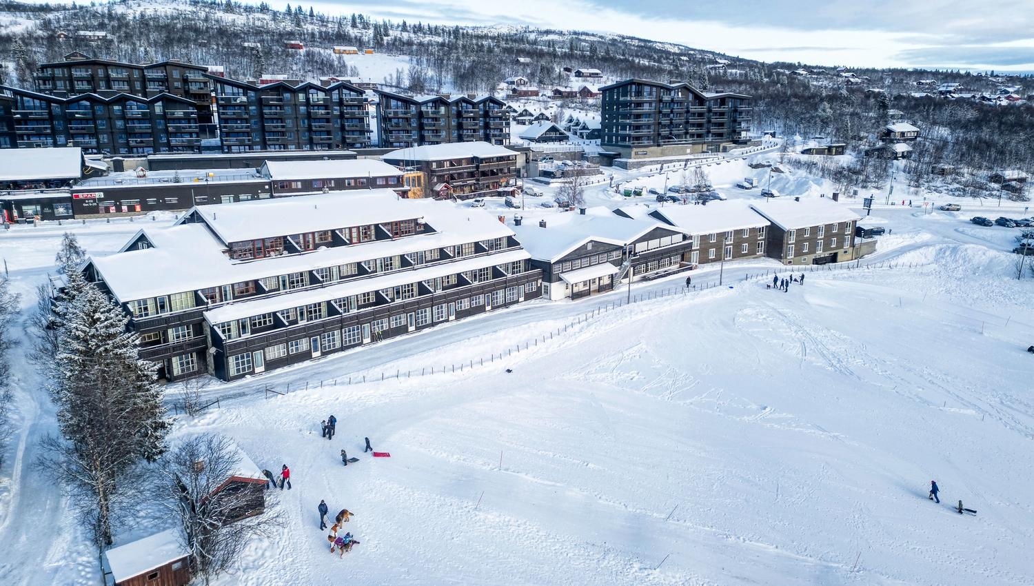 Dronebilde av Bergo Rom på vinteren. Man kan se barn som aker på jordet en fin vinterdag.