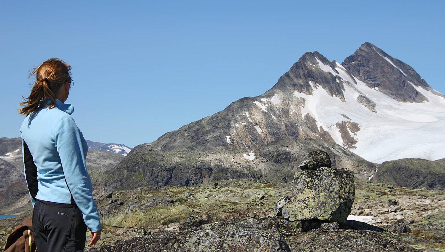 En dame med hestehale og blå jakke står og beundrer kvasse fjell.