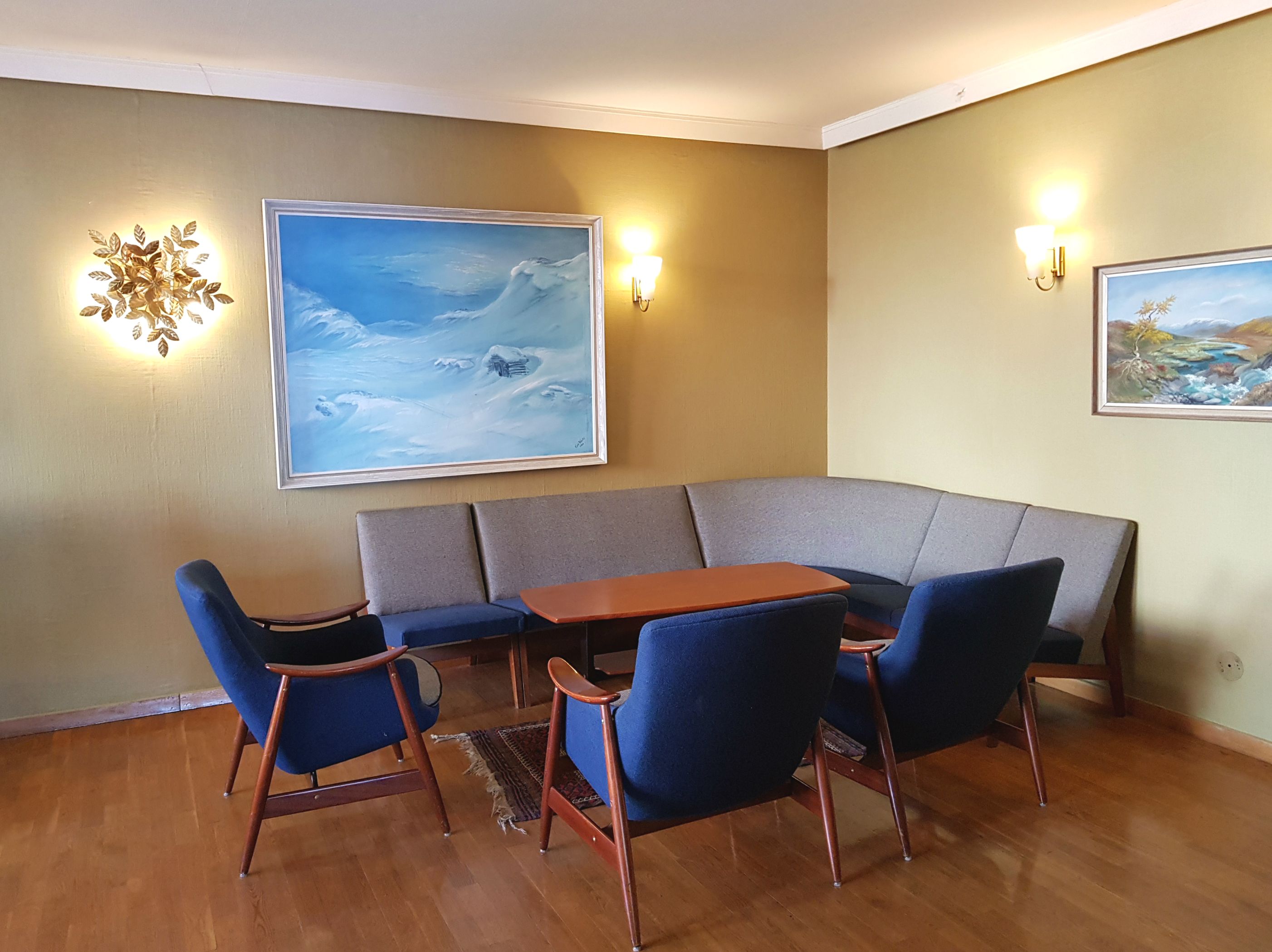 En sofa, noen stoler og et bord, med malerier hengende på veggene over.