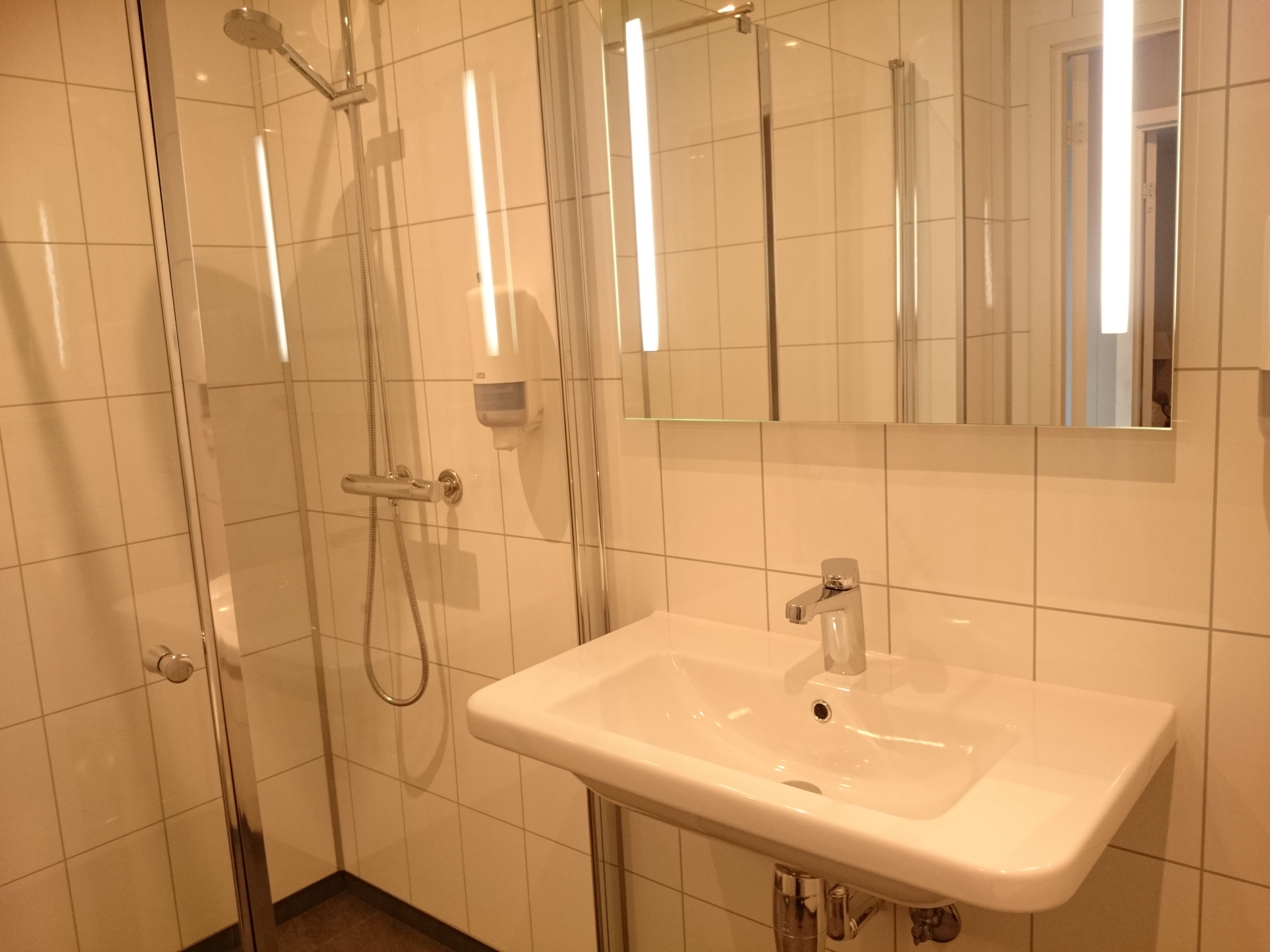 Reint og moderne bad med dusjkabinett, flislagde vegger og god belysning på Ullensvang Gjesteheim.