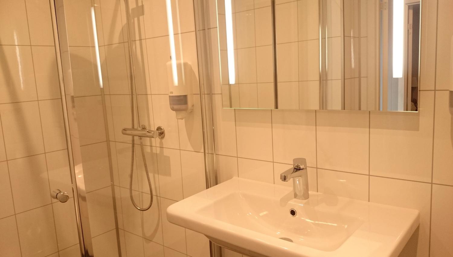 Reint og moderne bad med dusjkabinett, flislagde vegger og god belysning på Ullensvang Gjesteheim.