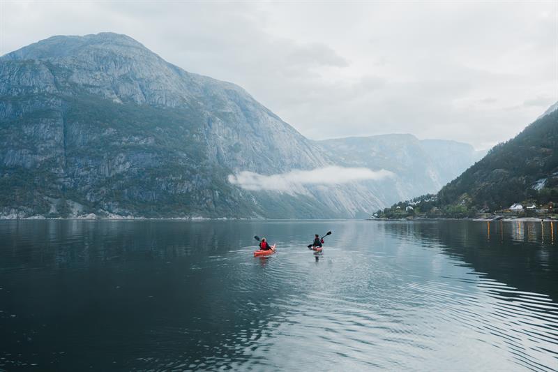 A couple kayakking on the fjord towards a large mountain.