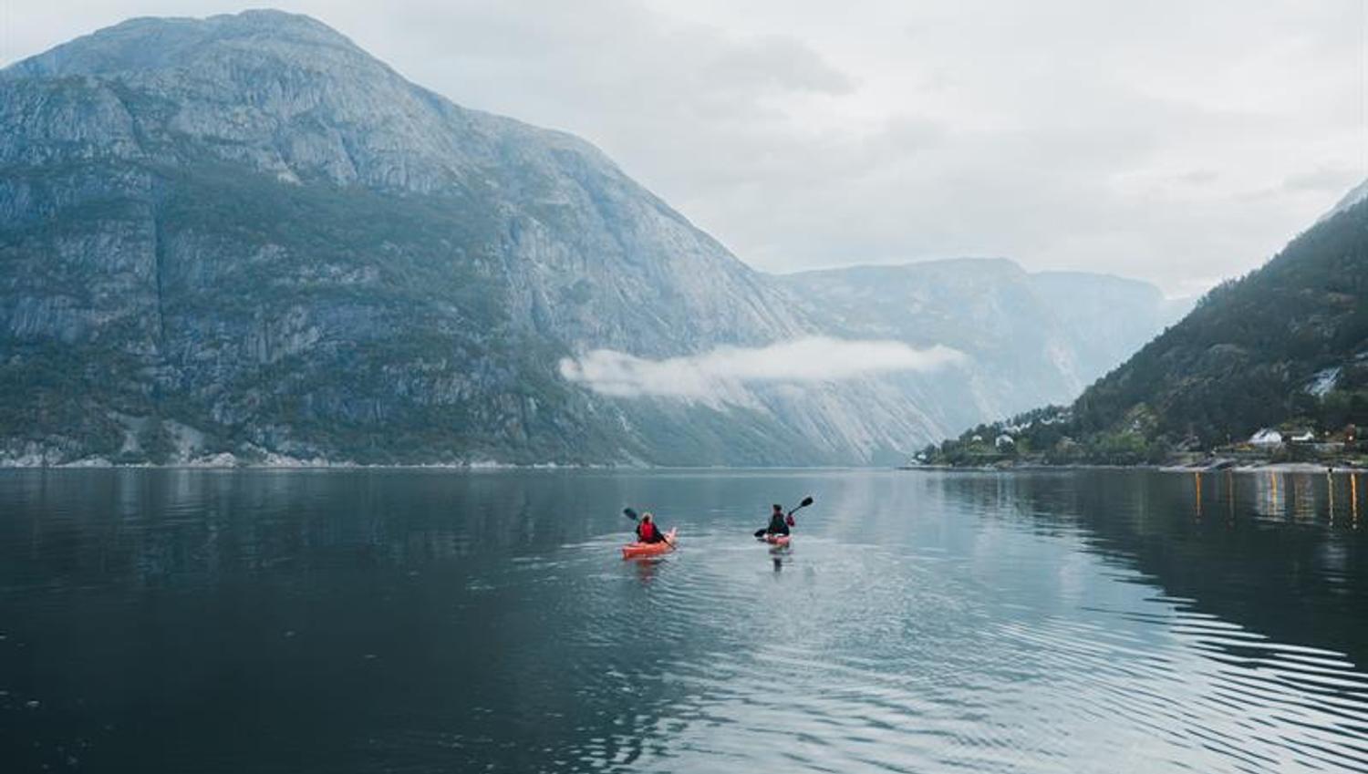 A couple kayakking on the fjord towards a large mountain.