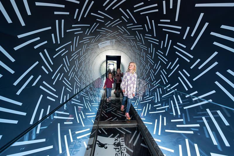 Barn går gjennom en speilbelagt tunnel med lysmønstre som gir en futuristisk og sanselig opplevelse.