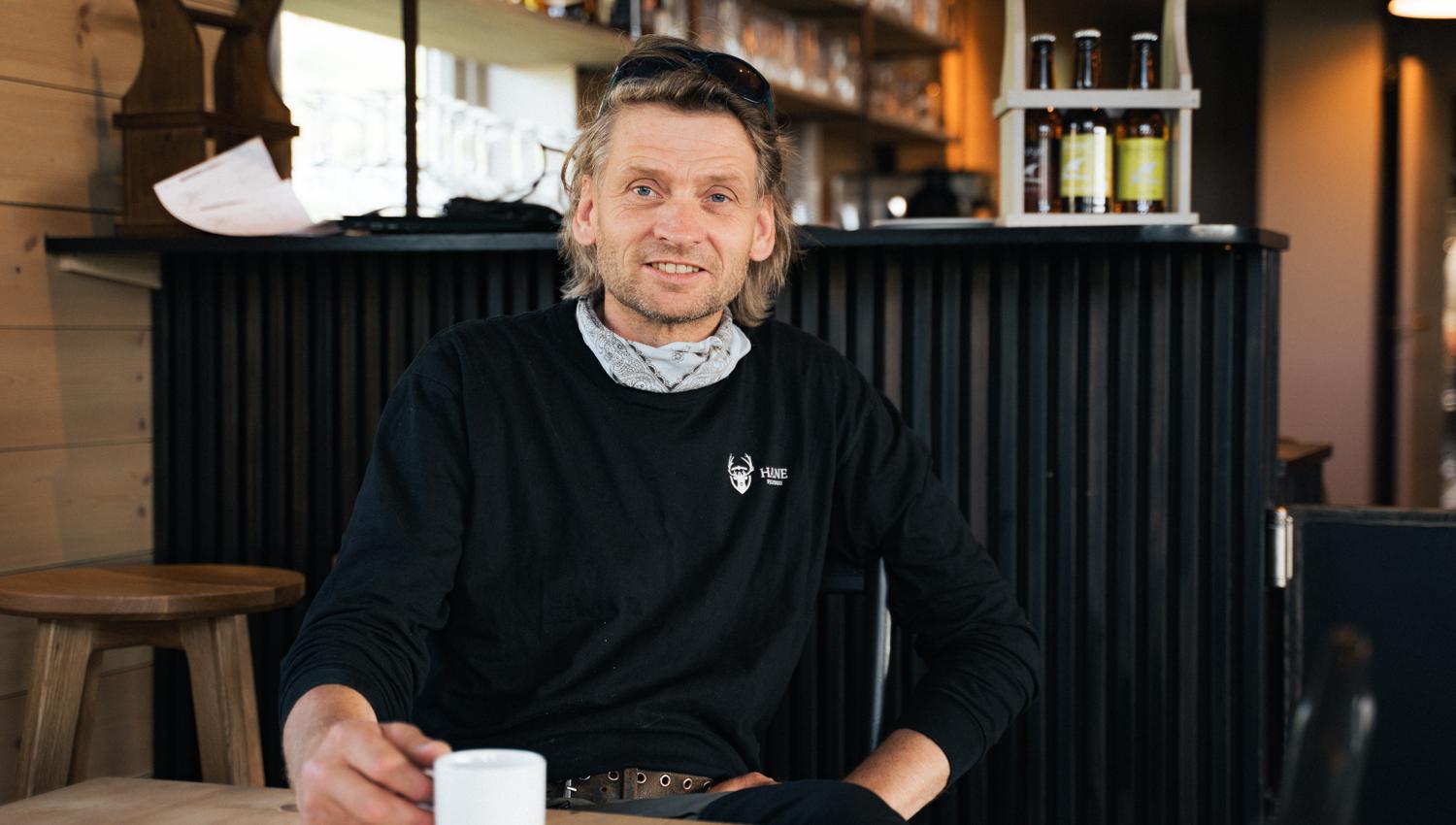 Eieren på Halne fjellstugu sitter ved et bord og holder en kopp kaffe.