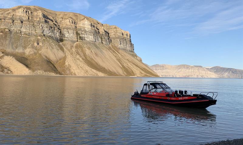 A RIB boat anchored on a shore with a fjord and a mountain in the background