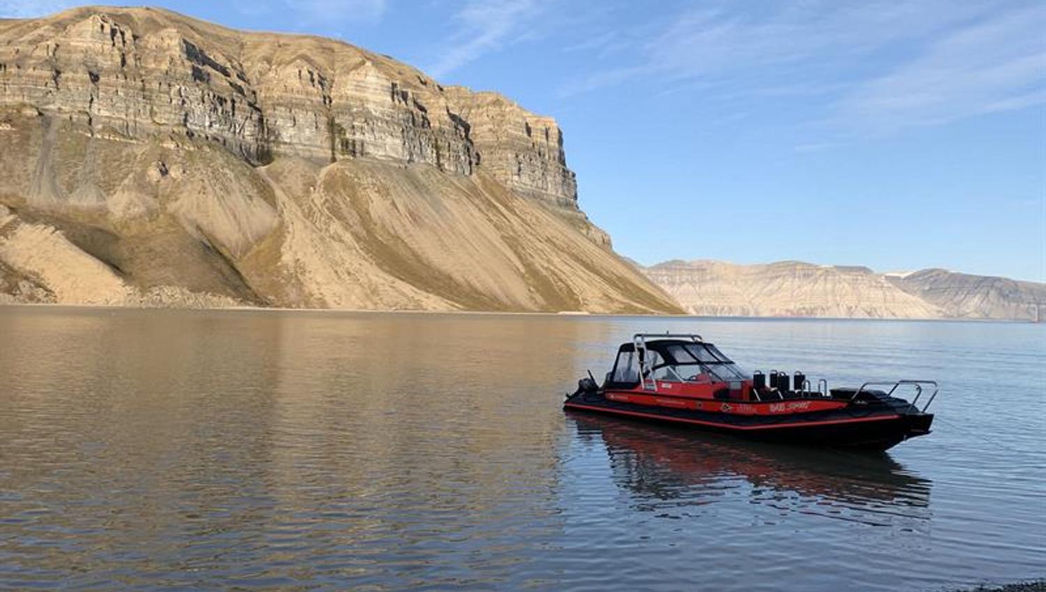 A RIB boat anchored on a shore with a fjord and a mountain in the background