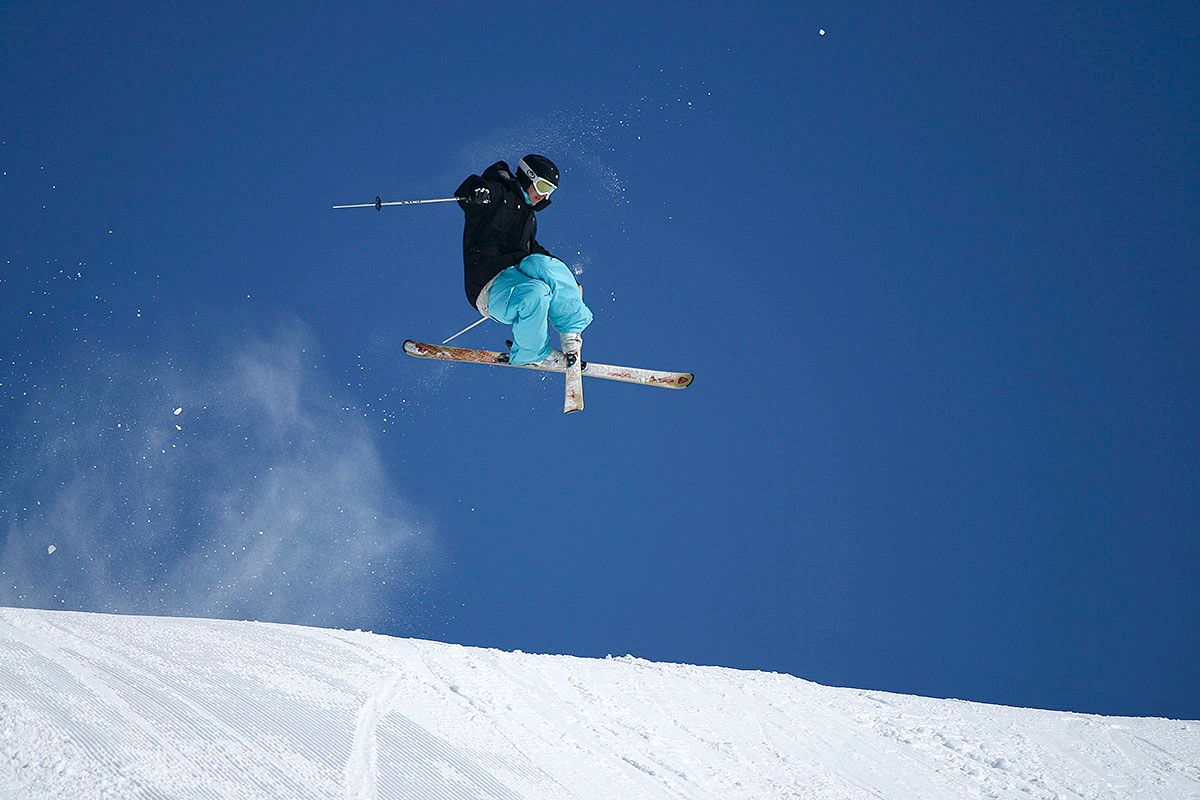 A skier jumps and crosses his skies. Blue skies in the backgound.