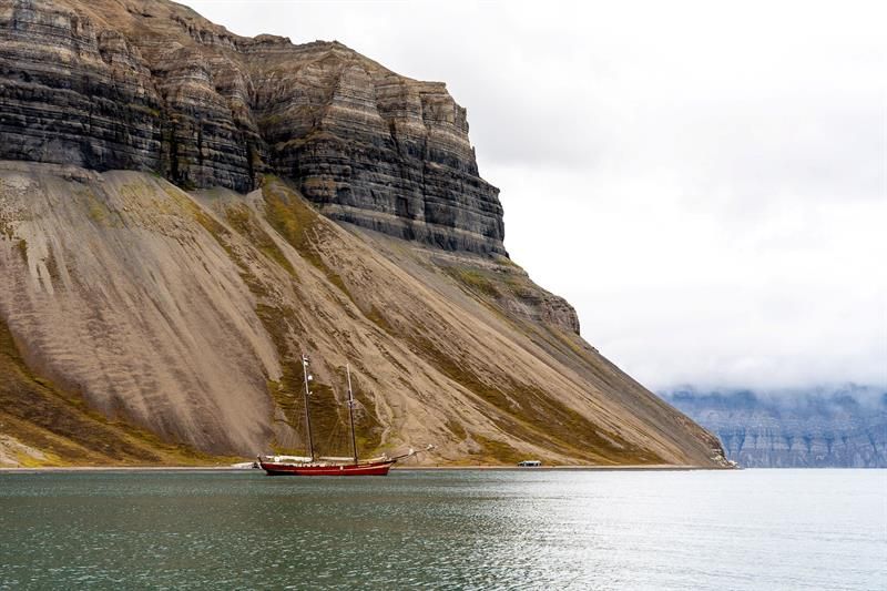 Rød seilbåt i fjord med bratte fjell på Svalbard.