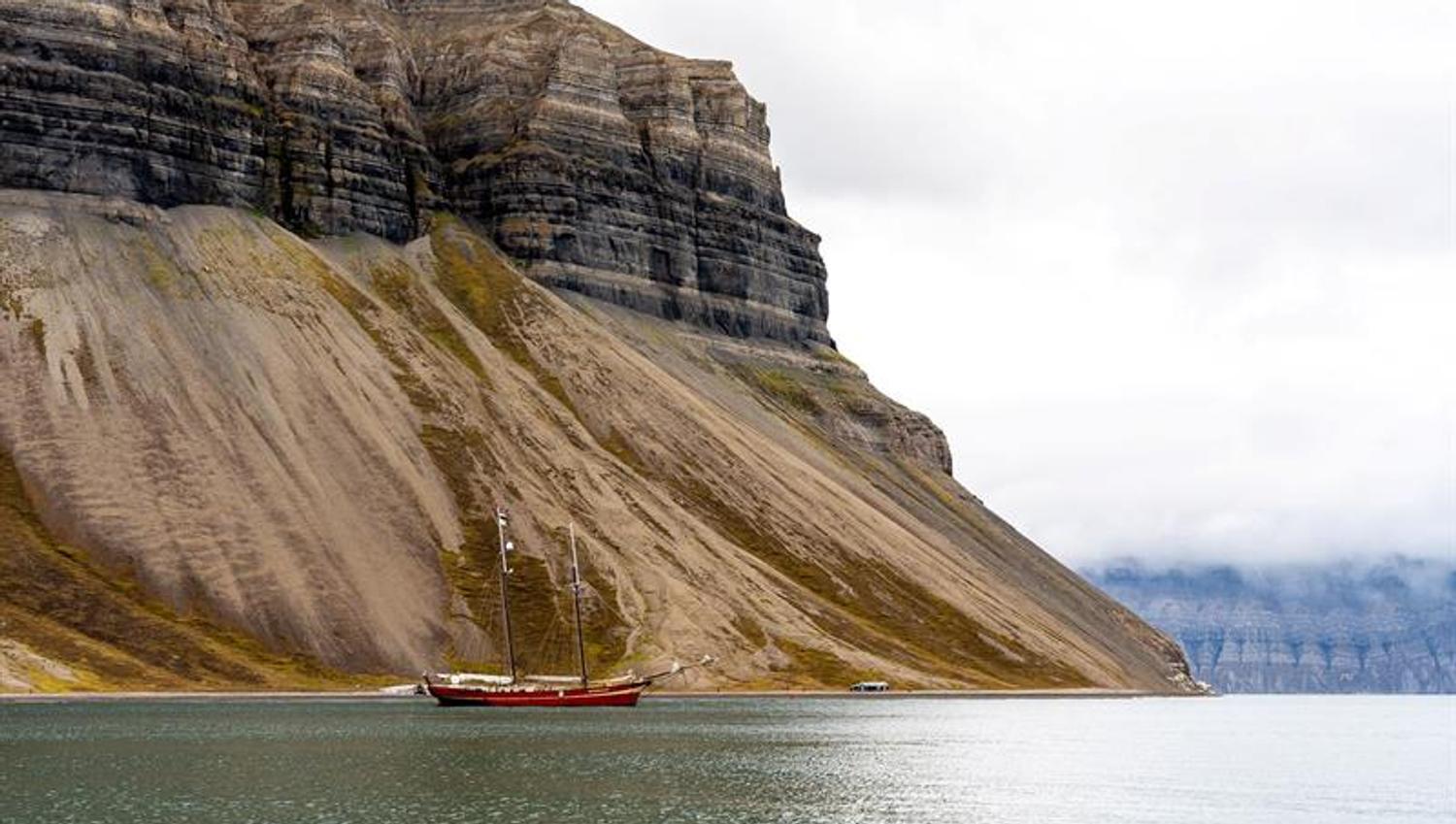 Rød seilbåt i fjord med bratte fjell på Svalbard.