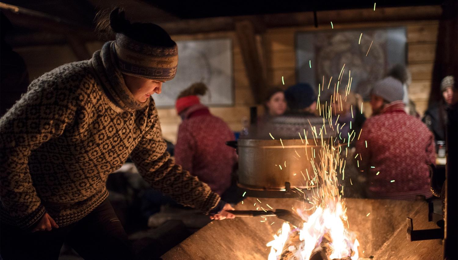 A host at Camp Barentz putting a log on a fire