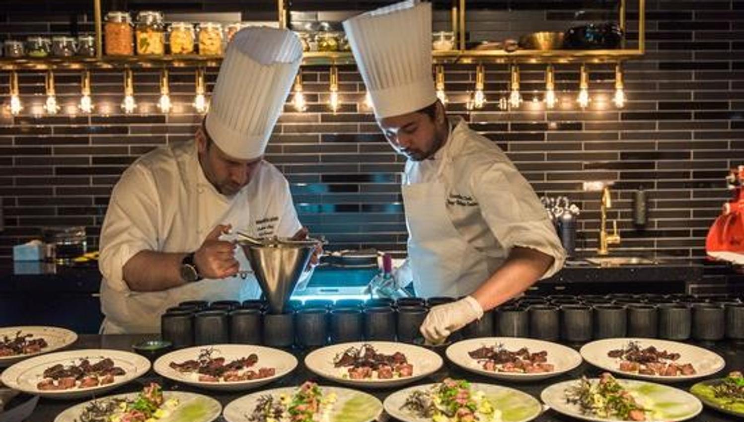 To kokker som forbereder matretter til servering på et kjøkken