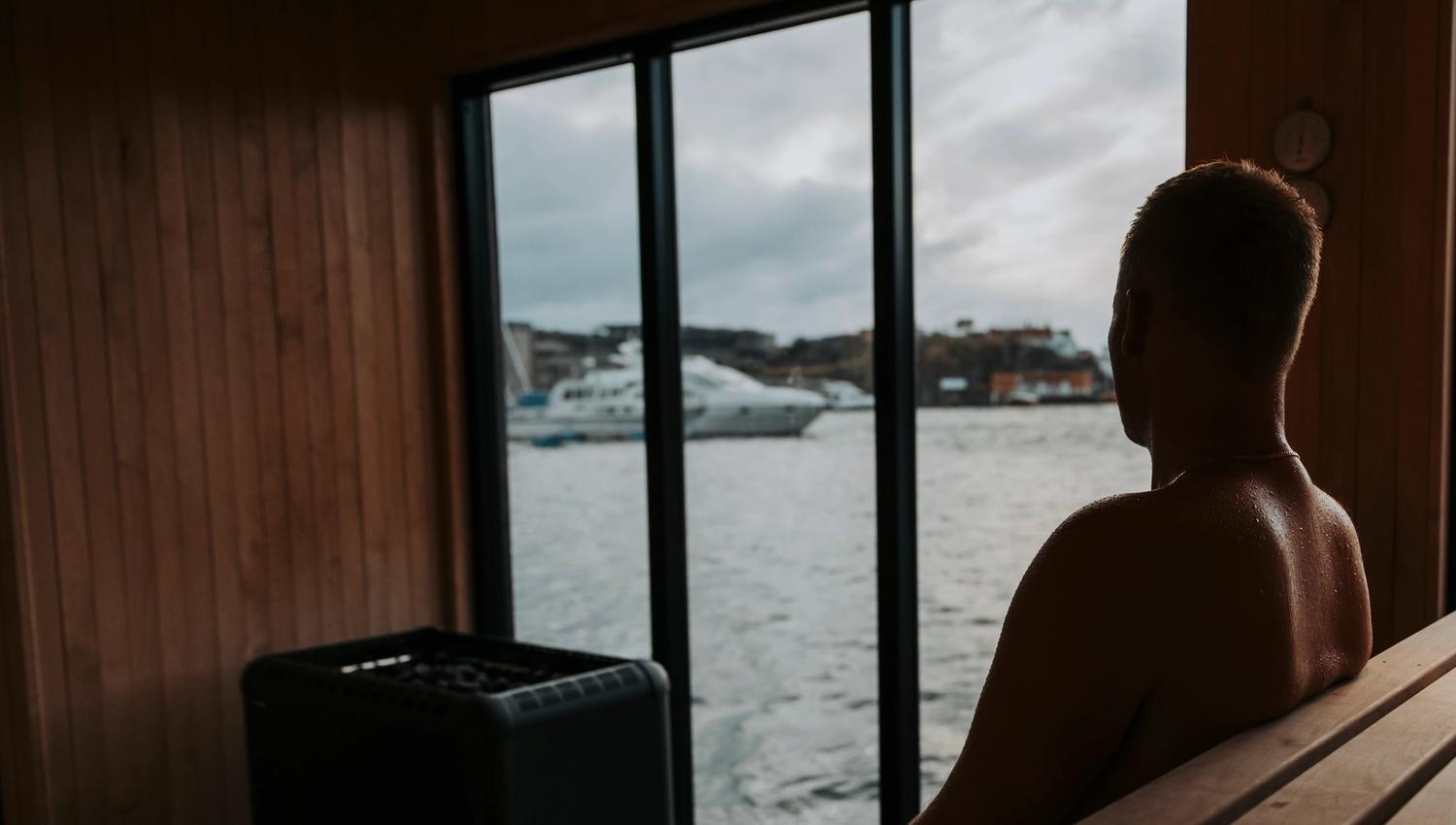 En mann som sitter inne i badstubåten Pysen og ser ut av vinduet