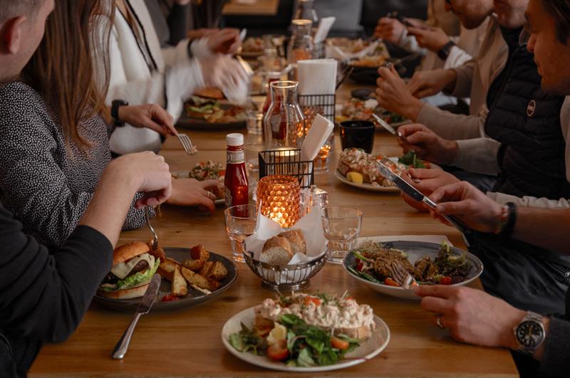 Guests gathered around a long table enjoying food and drinks in a warm, social restaurant atmosphere.