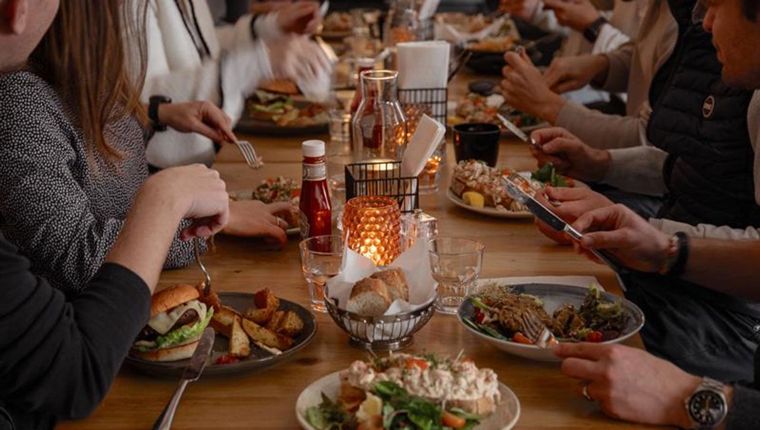 Guests gathered around a long table enjoying food and drinks in a warm, social restaurant atmosphere.