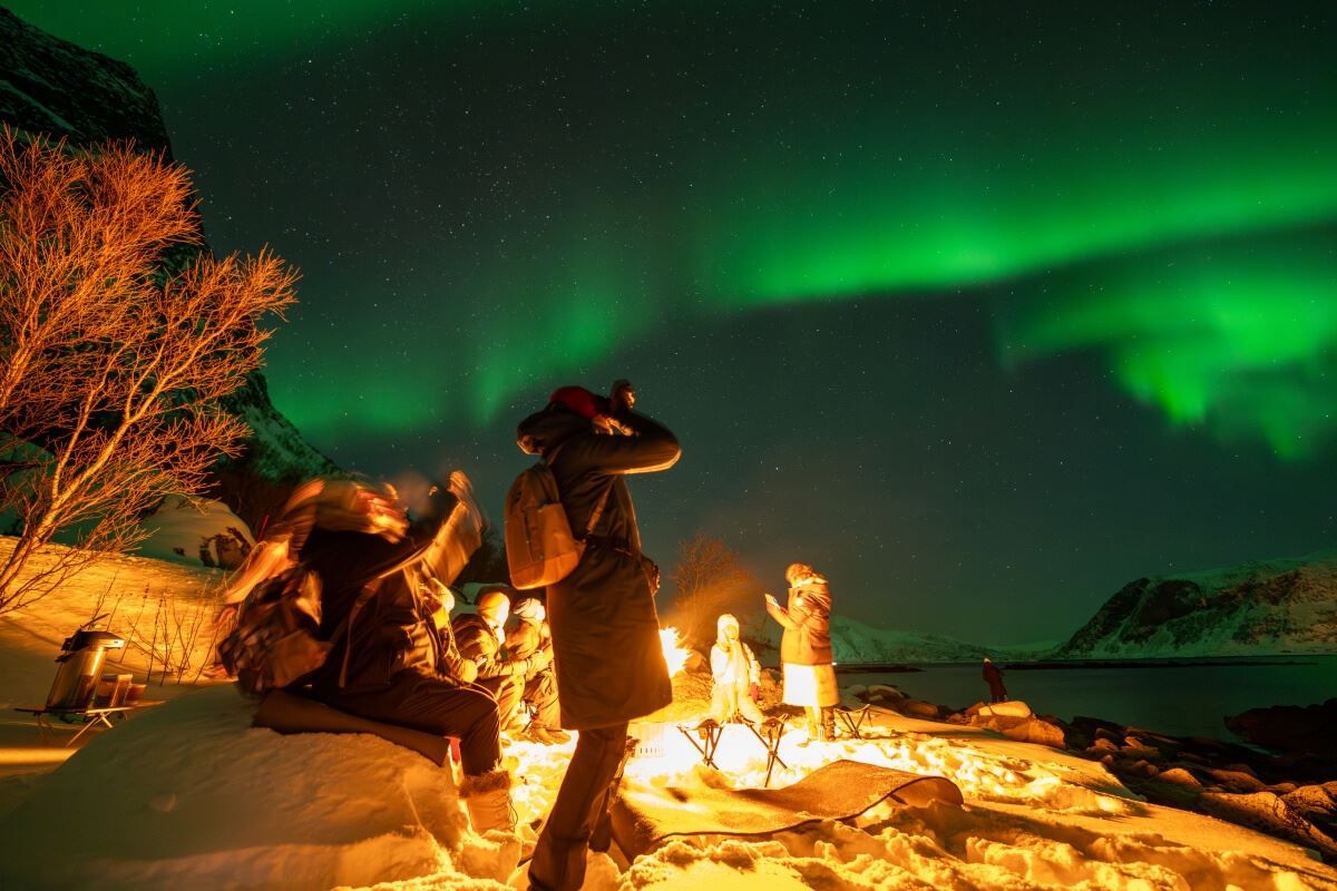 En gjest tar bilde av nordlyset ved siden av bålet