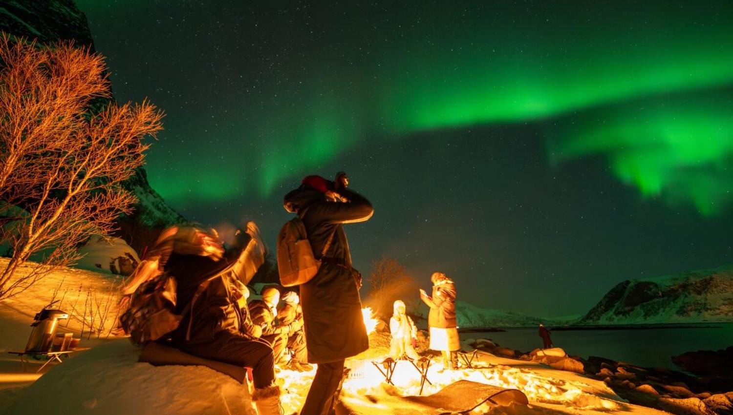 En gjest tar bilde av nordlyset ved siden av bålet