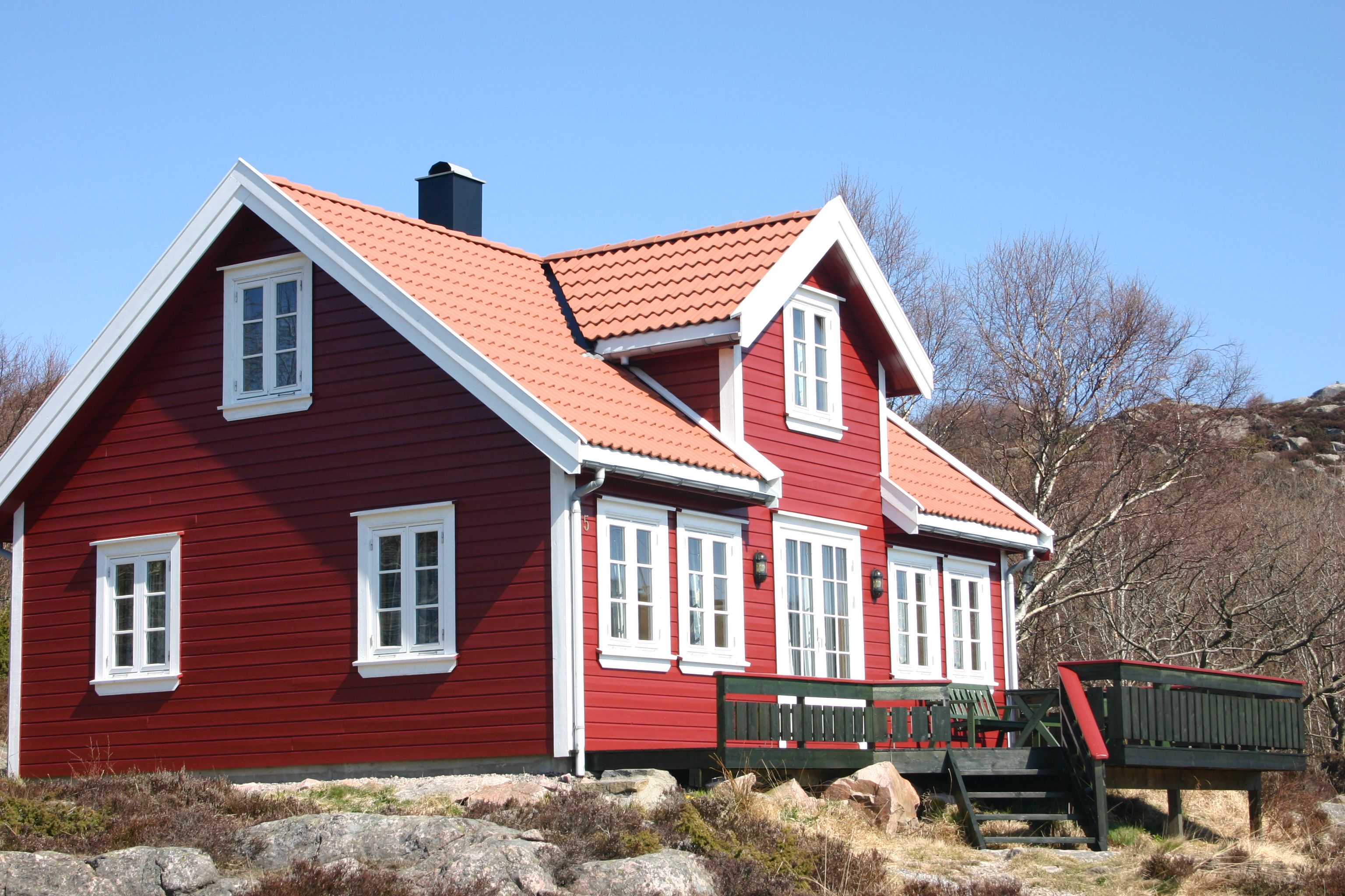 Lindesnes Camping og Hytteutleie - En stor rød hytte med hvite karmer, med grønn terrasse