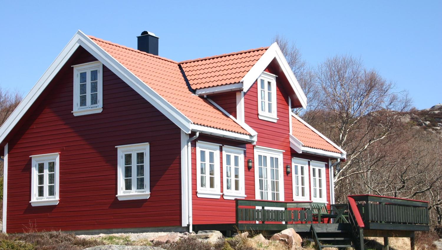 Lindesnes Camping og Hytteutleie - En stor rød hytte med hvite karmer, med grønn terrasse