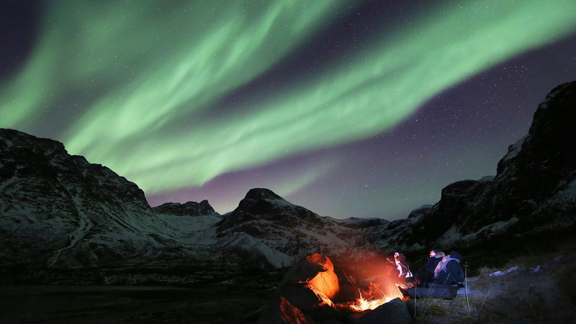 Guests sitting around a bonfire under the northern lights