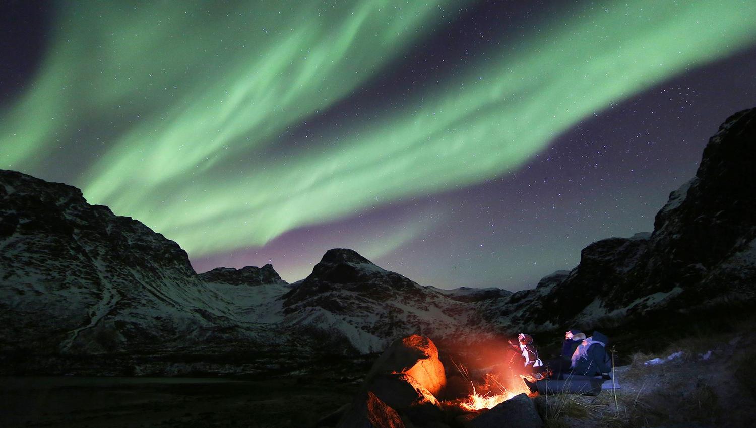 Guests sitting around a bonfire under the northern lights