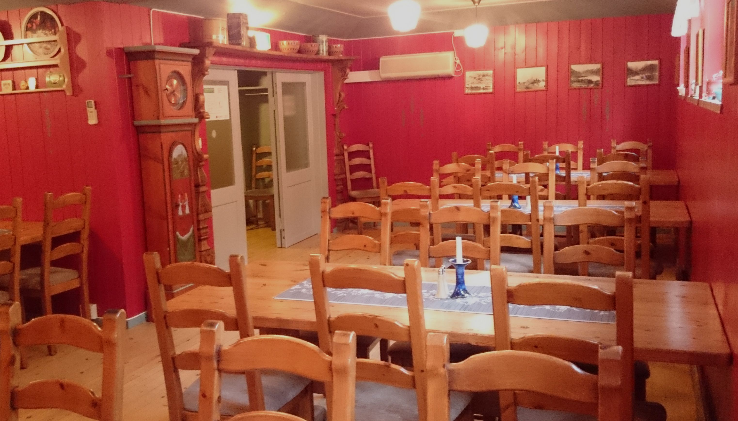 Romslig spisesal med langbord og trestolar på Ullensvang Gjesteheim, dekorert med historiske detaljar og varme fargar.