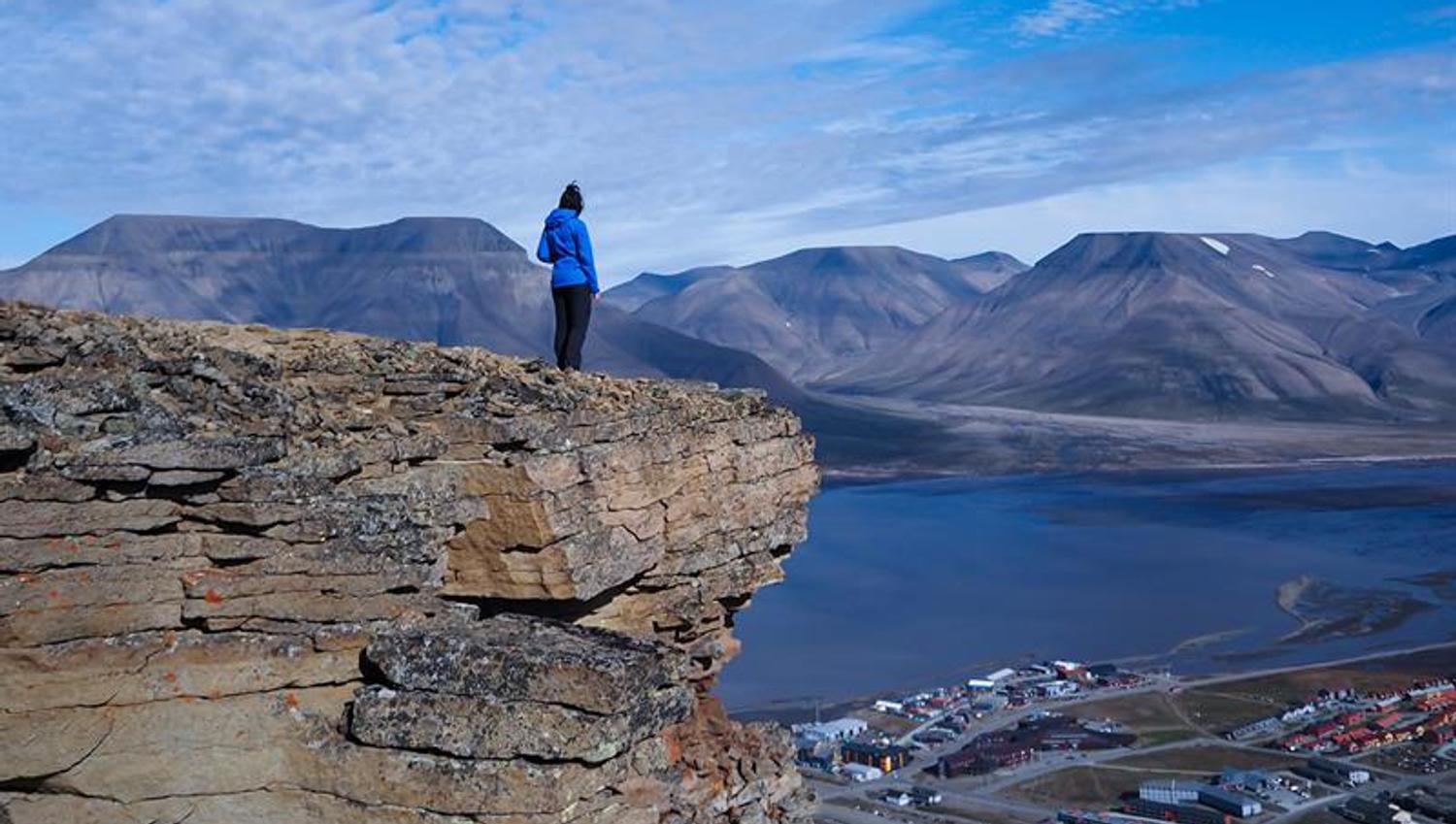 person standing on mountaintop looking at the view over town