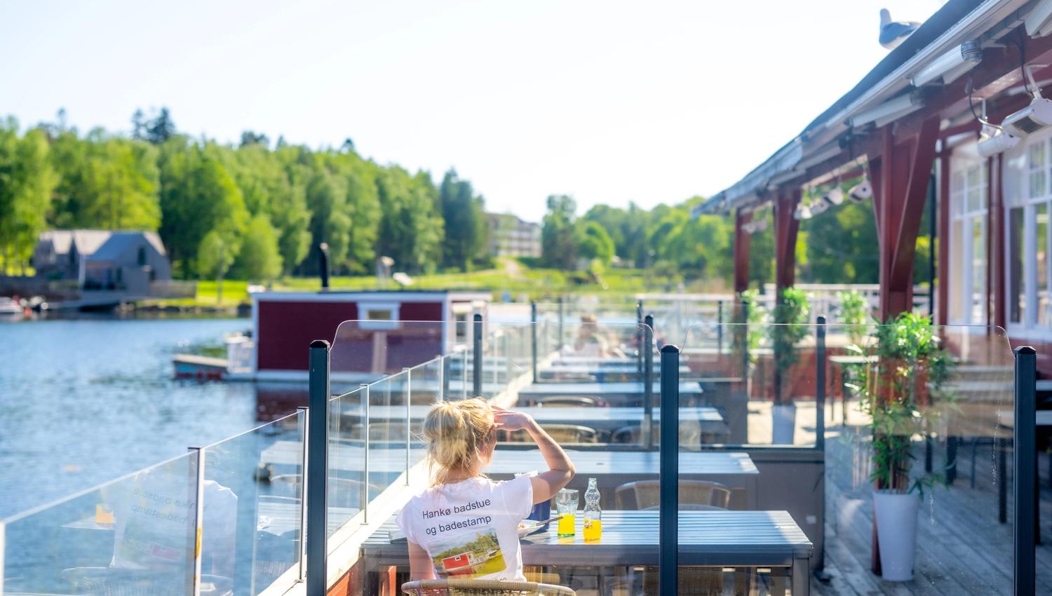Outdoor dining area by the waterfront, guests enjoying meals with a view of the marina and lush surroundings.