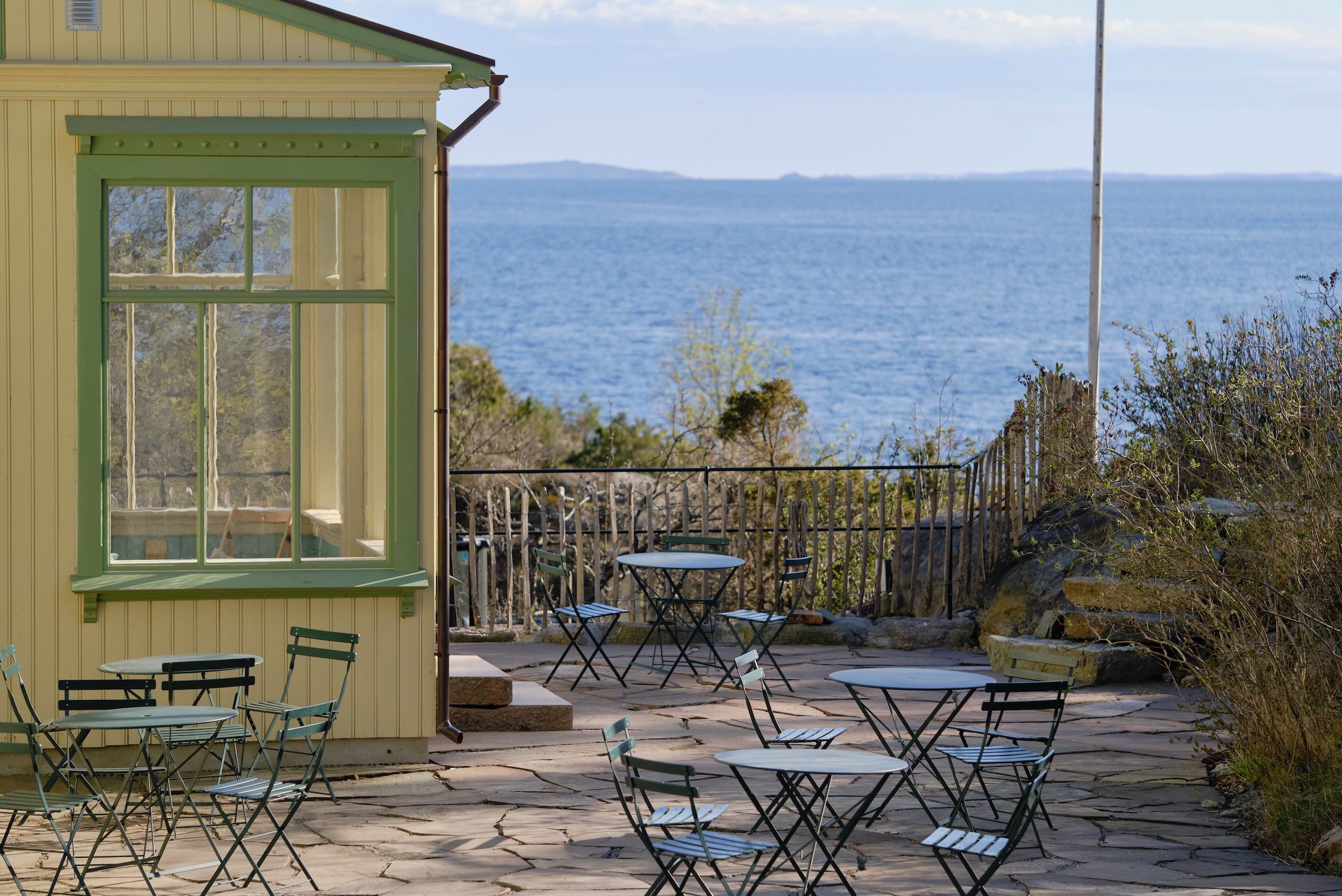 Gult hus med vindu sjøutsikt og terrasse med bord og stoler