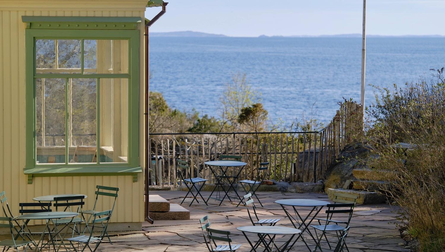 Gult hus med vindu sjøutsikt og terrasse med bord og stoler