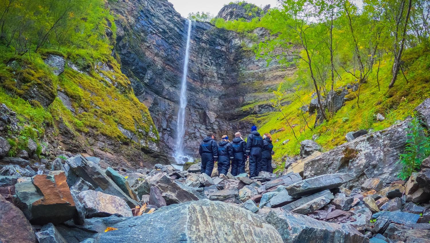 Experience the tranquility of nature as a stunning waterfall flows down majestic cliffs. Adventurers clad in jackets explore the rocky terrain, surrounded by vibrant foliage and the sounds of cascading water. A perfect spot for those seeking adventure and