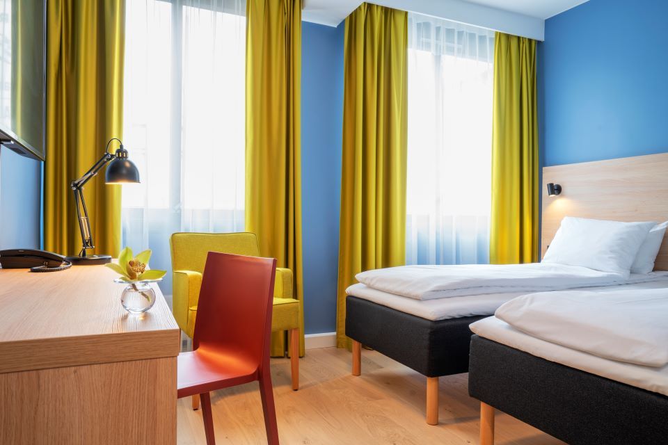 Room interior: Two beds, yellow armchair, wooden desk, red chair, blue-painted walls and yellow curtains.
