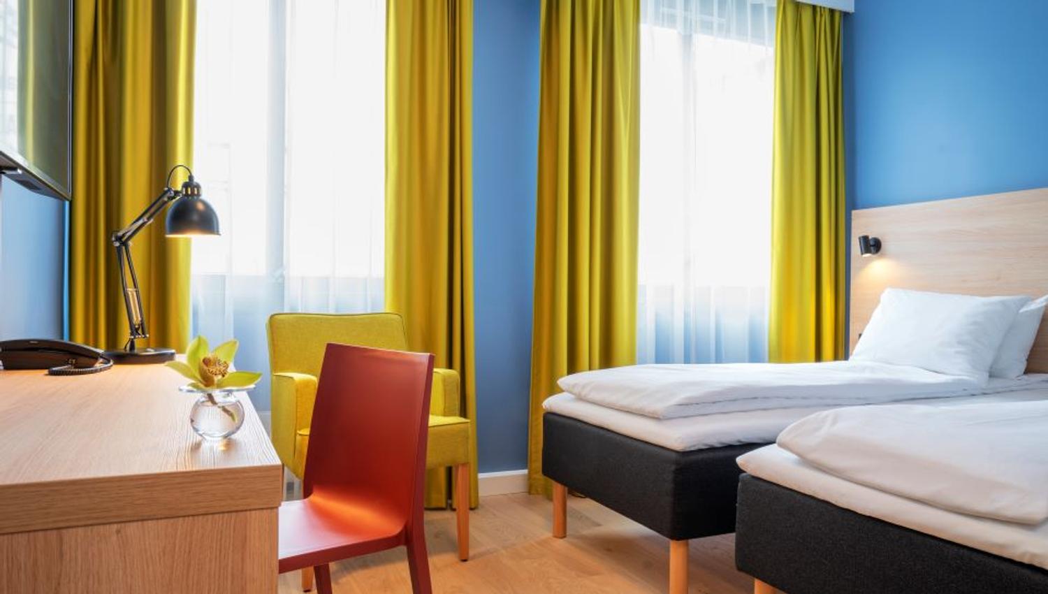 Room interior: Two beds, yellow armchair, wooden desk, red chair, blue-painted walls and yellow curtains.