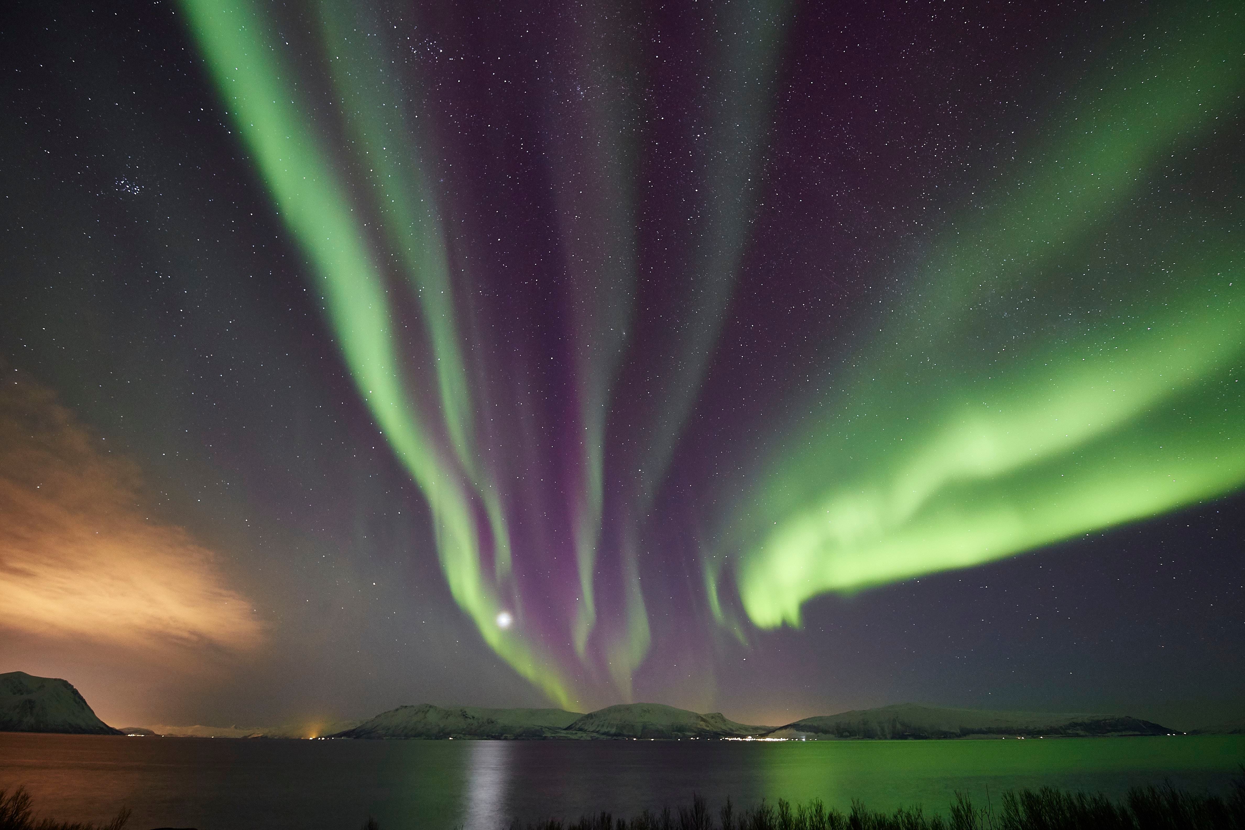 et nordlys som går parallelt på himmelen over havet mot land 