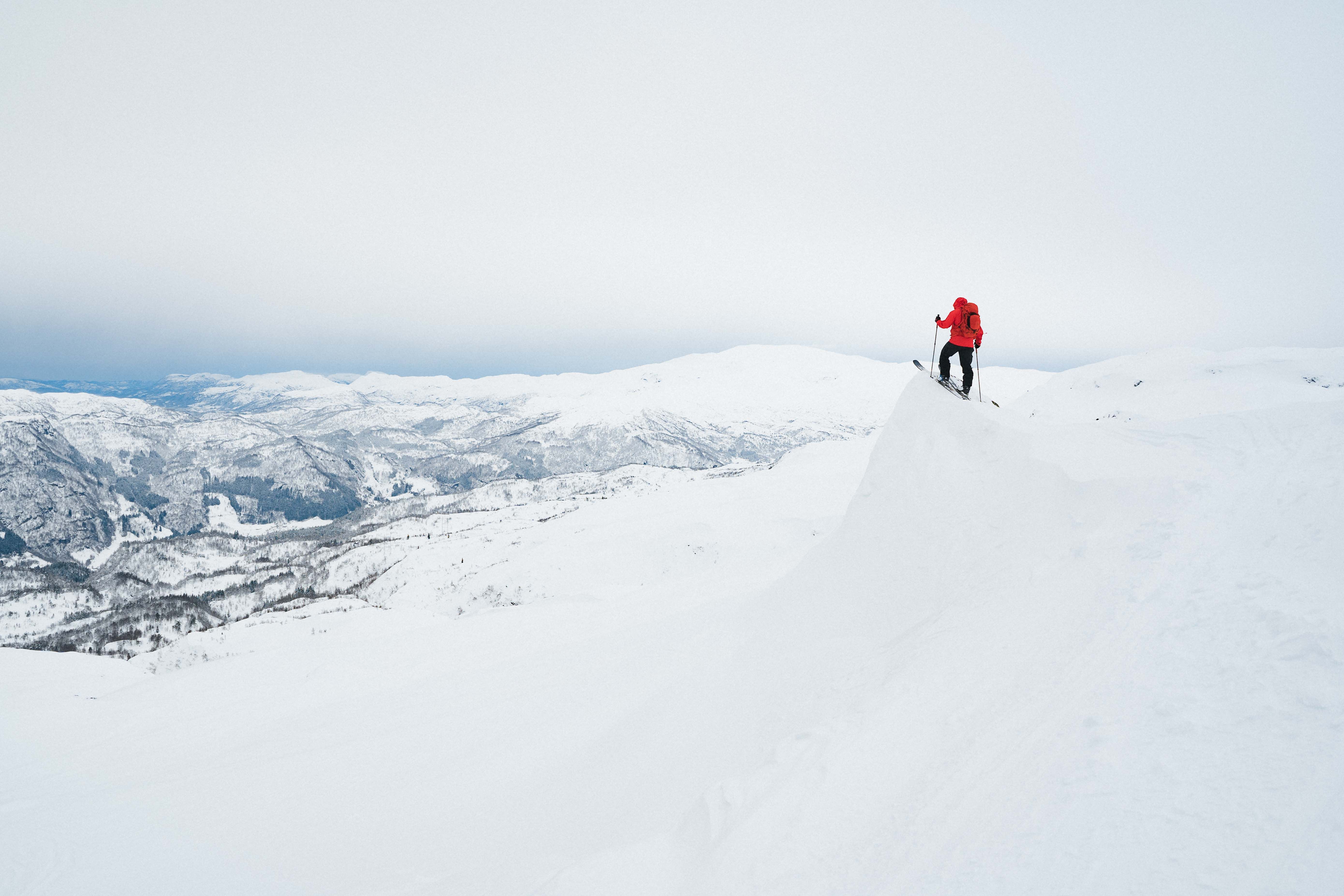 En person på ski står på en kant og ser utover et snødekket landskap.