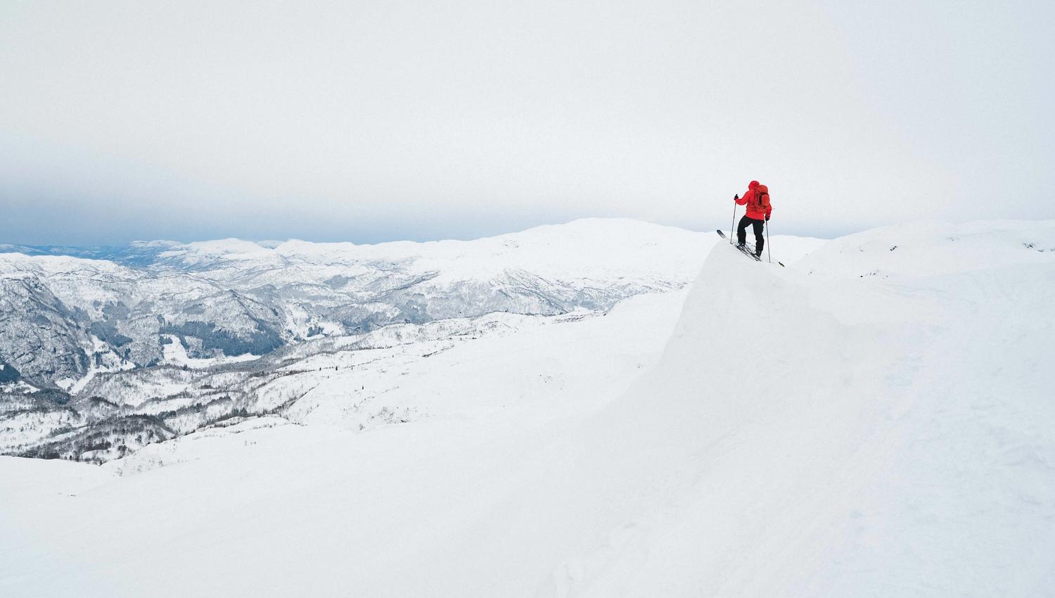 En person på ski står på en kant og ser utover et snødekket landskap.